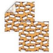 Scattered Hebrew 'hello my name is' nametags - brown on yellow/orange gingham