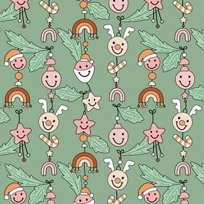 Cozy Christmas kawaii decoration - Happy holidays seasonal smiley design with raindeer bells stars rainbows and christmas ornaments hanging on branches pink orange on sage green