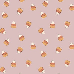 Small hand drawn scattered candy corn in yellow, burnt orange, and cream on a mauve pink background
